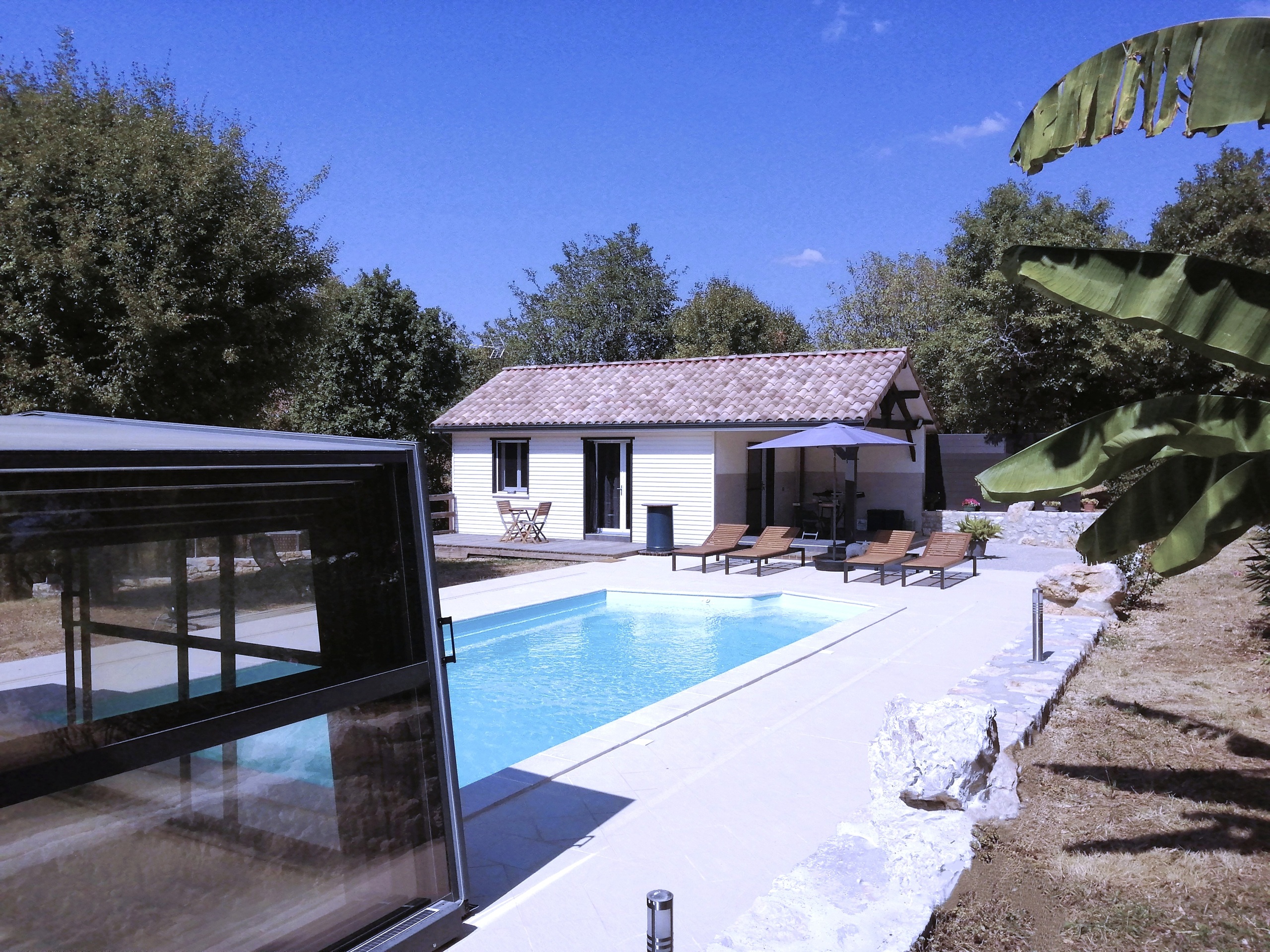 Piscine du gîte naturiste DACANIRO avec l’abri replié sur la gauche et le gîte sans panneaux photovoltaïques