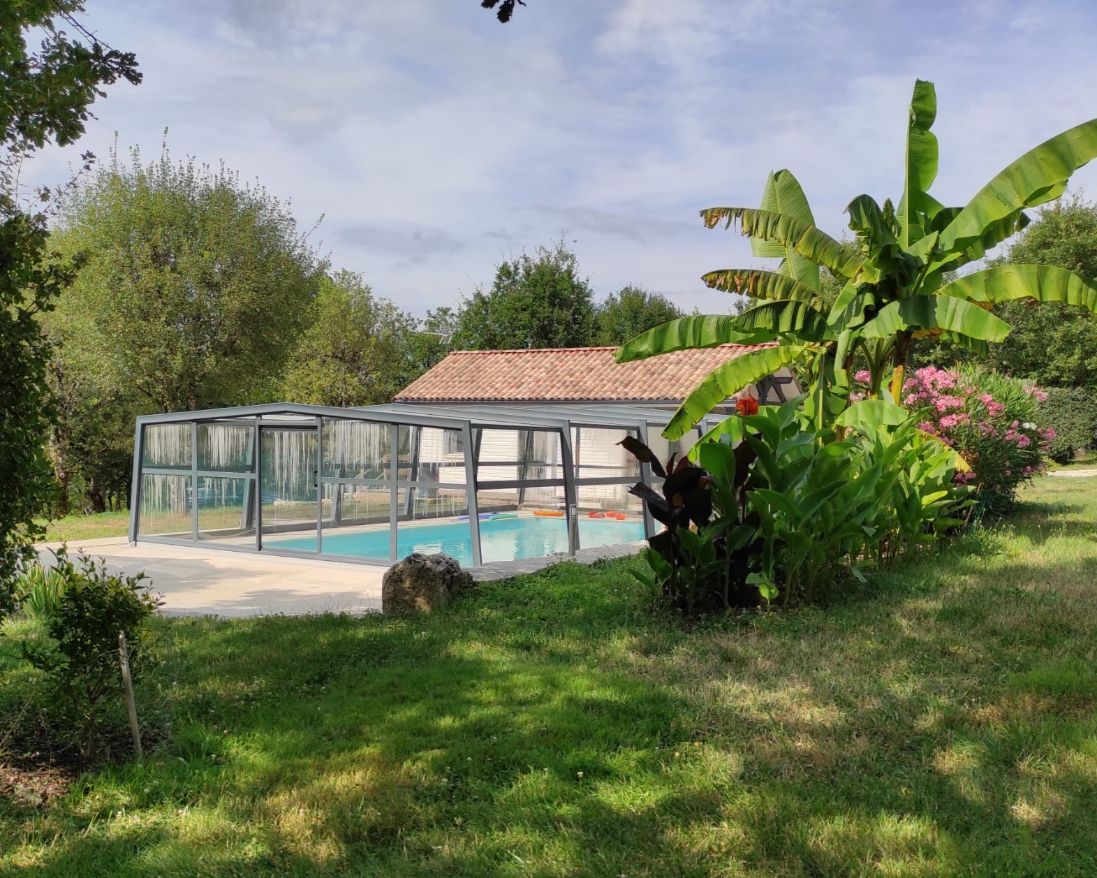 Piscine couverte du gîte naturiste DACANIRO avec son abri et la végétation luxuriante de juillet