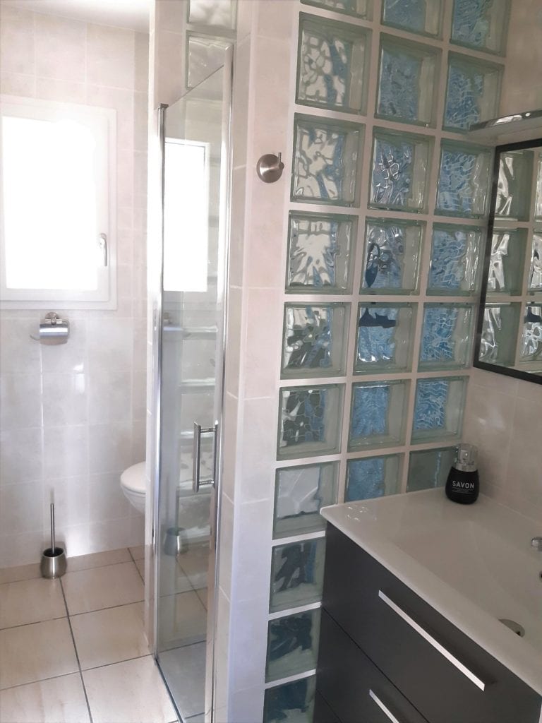 Salle d’eau du gîte avec douche italienne, vasque et tiroirs, WC suspendu, placard de rangement et fenêtre avec voilage