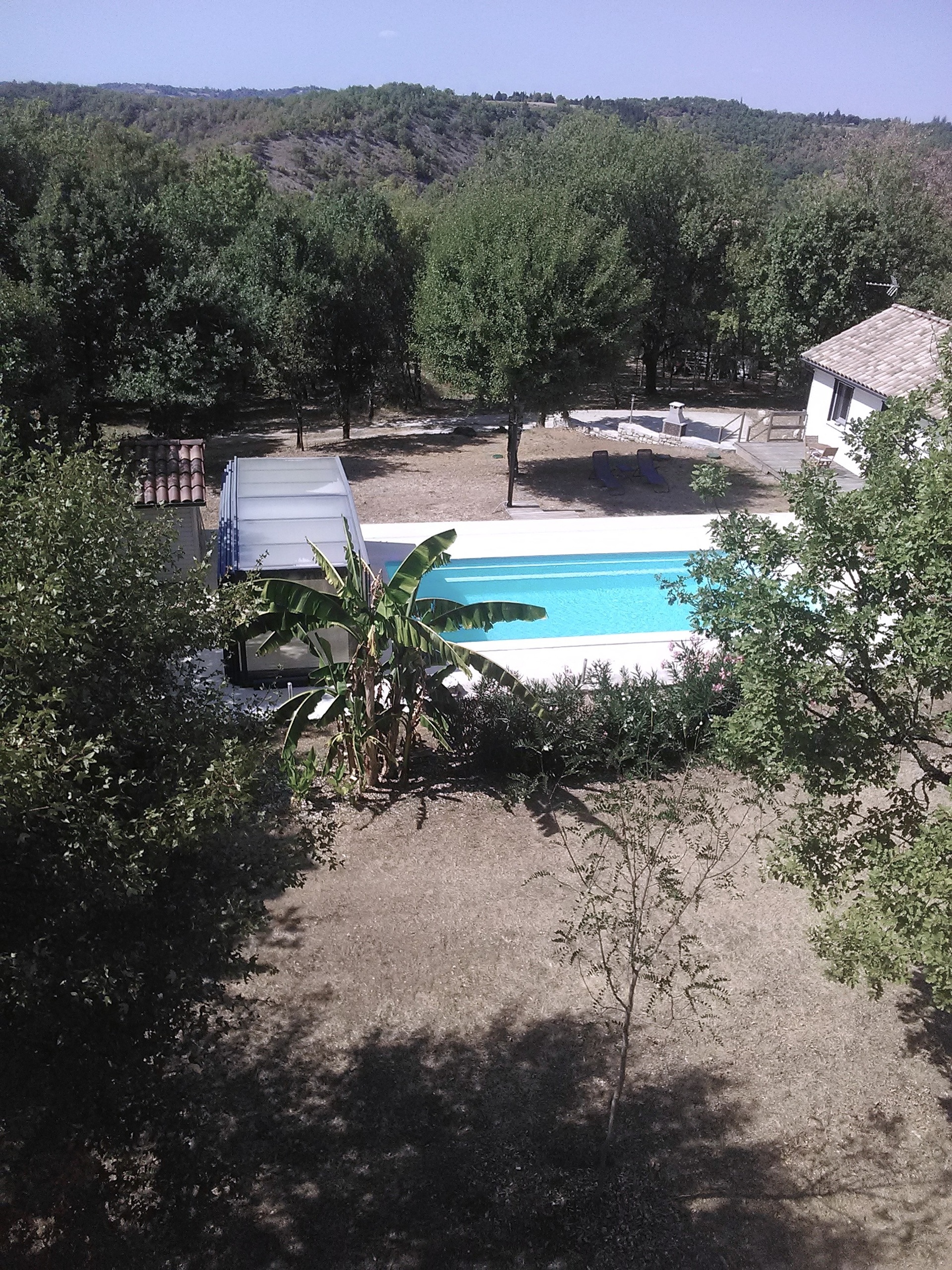Vue aérienne du gîte naturiste DACANIRO avec la piscine en contrebas, la forêt et la colline au loin
